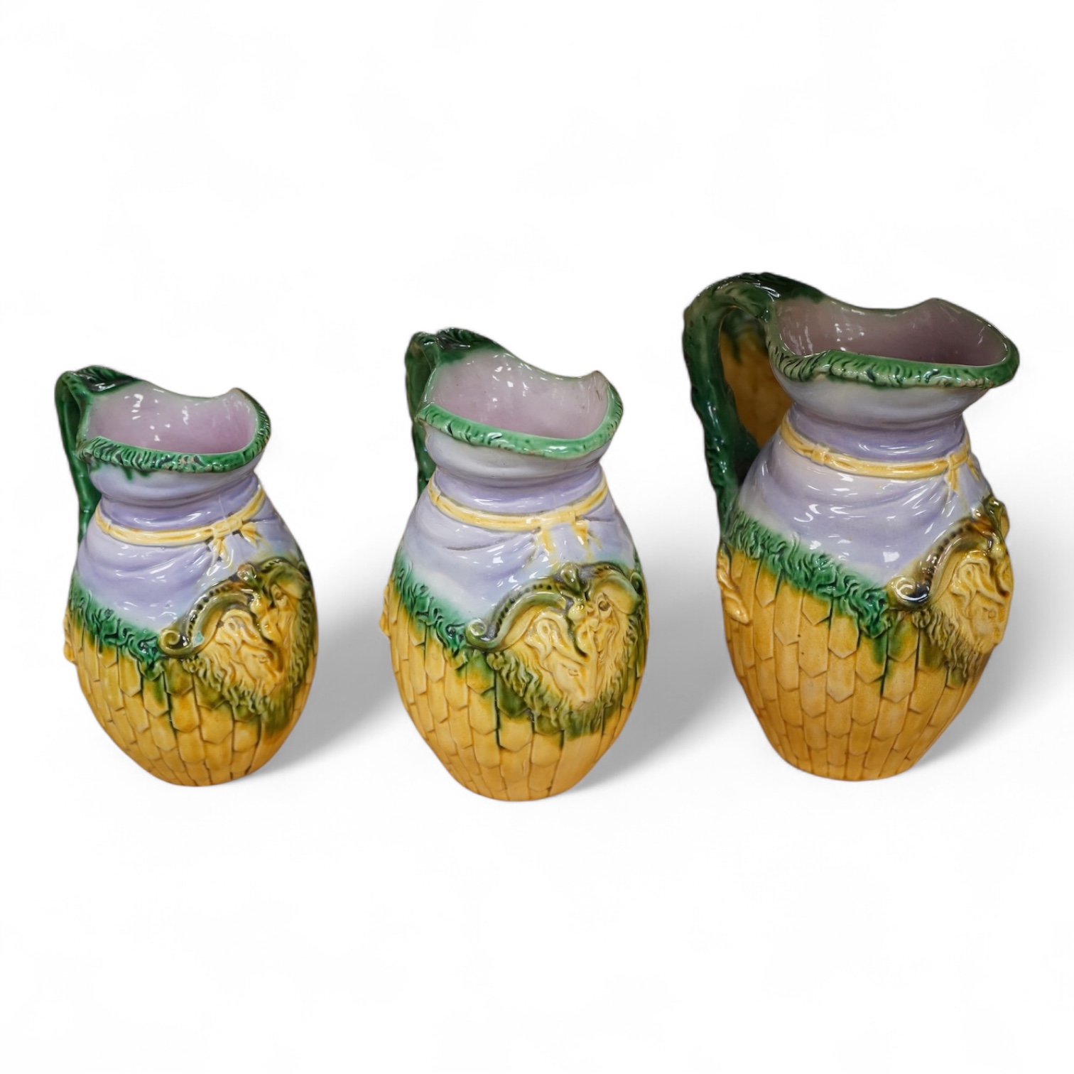 A graduated set of three maiolica ram decorated jugs, tallest 23cm high.